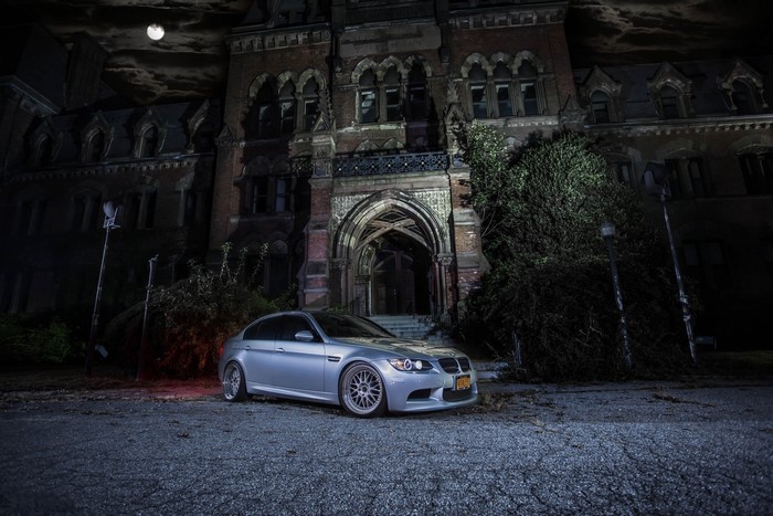 Silver BMW M3 E90 parked at night in front of an old building