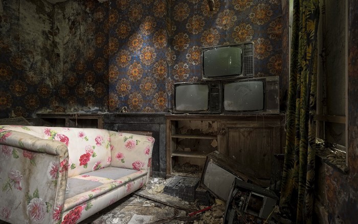 Abandoned room with floral sofa and old TVs