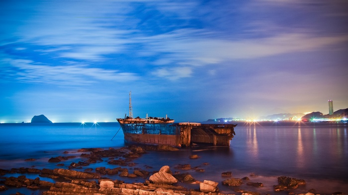 Shipwreck at night with distant city lights