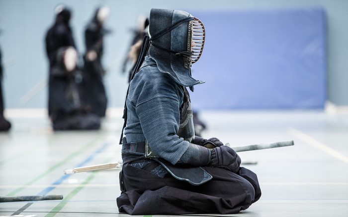 Kendo practitioner in protective gear sitting on the floor