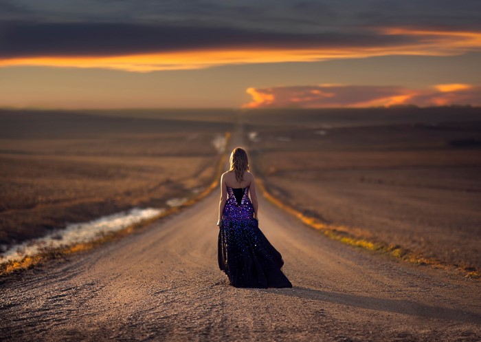 Woman in a sequined dress on a road at sunset