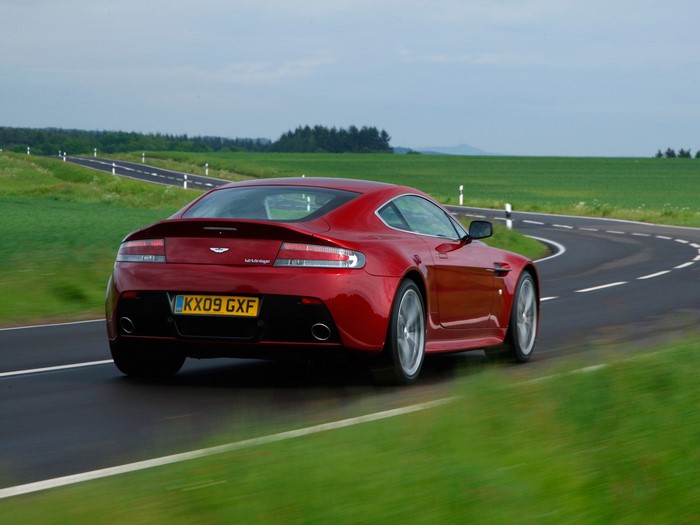 Red Aston Martin V12 Vantage driving on a winding road