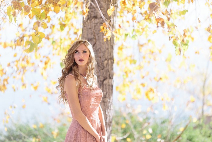 Blonde girl in a pink dress under autumn leaves