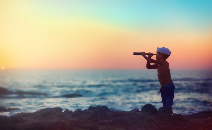 Boy with spyglass on beach at sunset