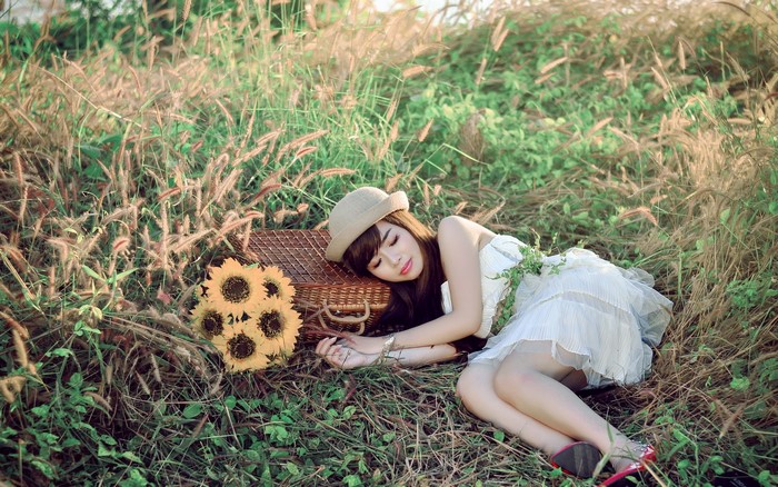 Asian girl in hat sleeping in grass with sunflowers