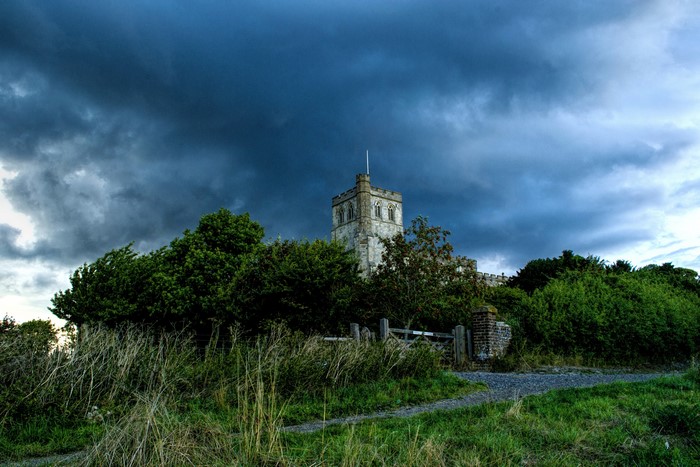 Church tower behind trees under stormy sky