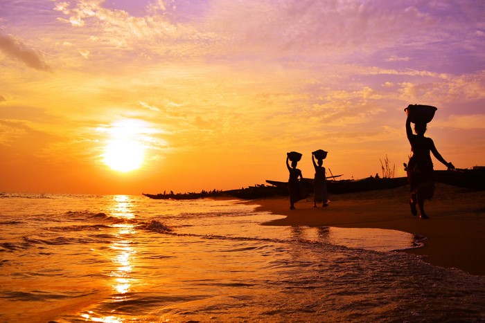 Sunset over the sea with people carrying baskets