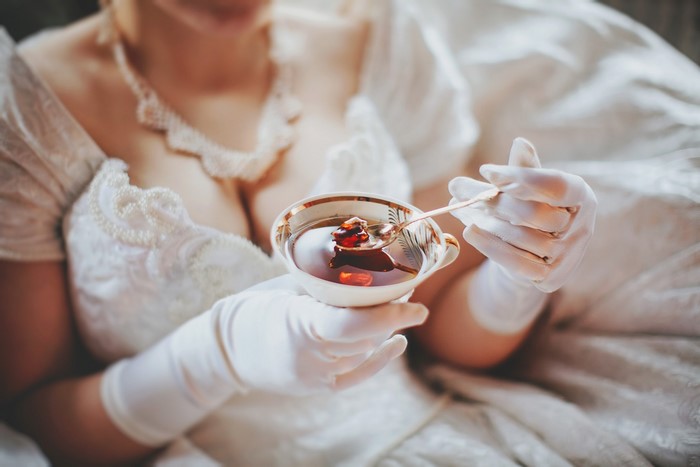 Bride in white dress holding a cup of tea with jam