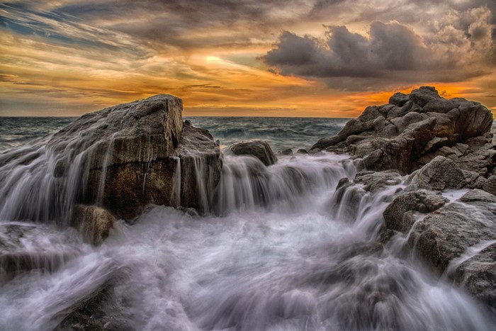 Sunset Over Rocky Shore with Flowing Waves