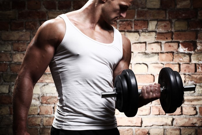 Man lifting dumbbell in white singlet