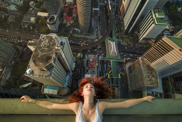 Redhead girl lying on skyscraper roof overlooking city
