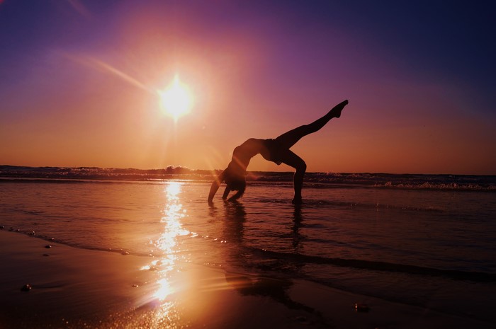 Gymnast performing a bridge pose on the beach at sunset