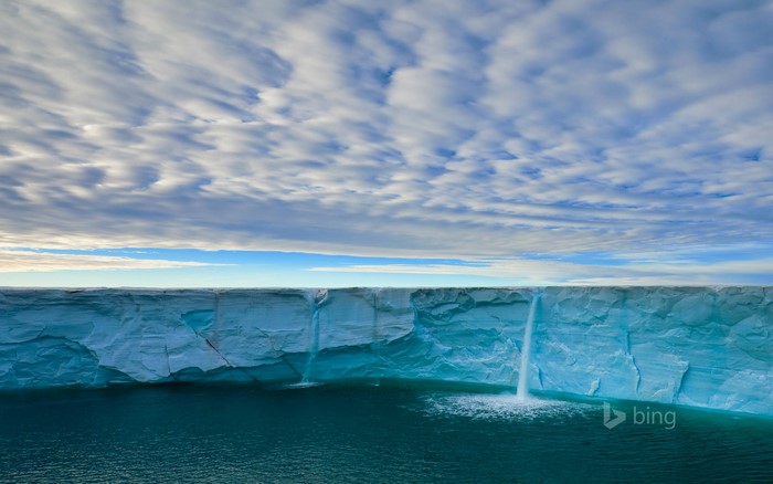 Waterfalls cascading from a glacier into the sea under a cloudy sky