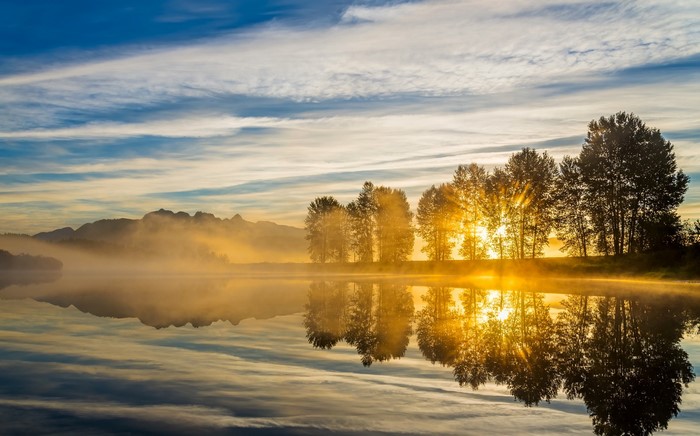 Sunrise over a misty lake with trees and mountains