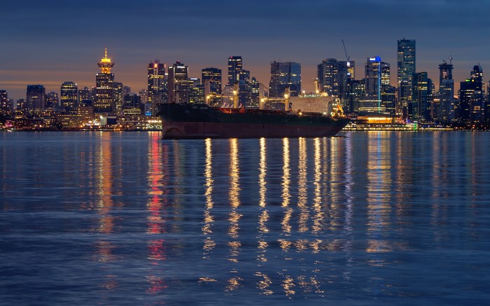 Cargo ship in front of Vancouver skyline at night