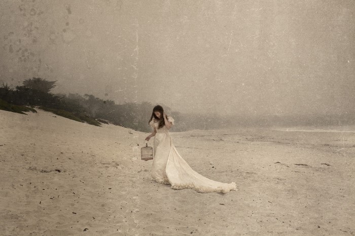 Woman in a white dress holding a birdcage on a beach
