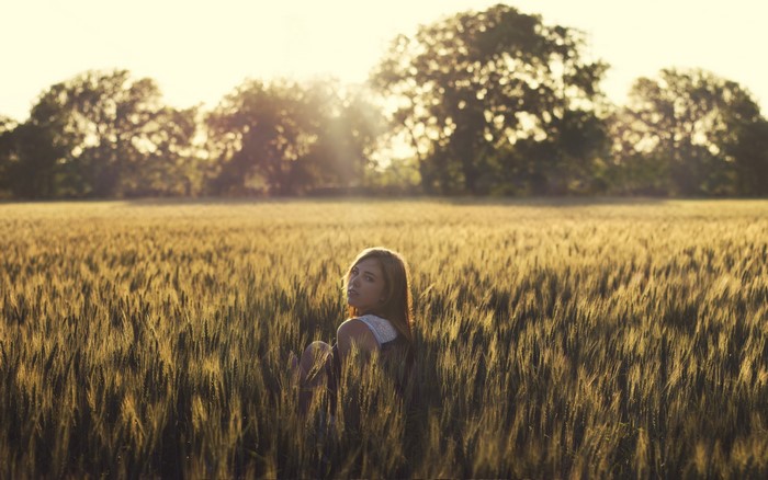 Girl sitting in a wheat field at sunset