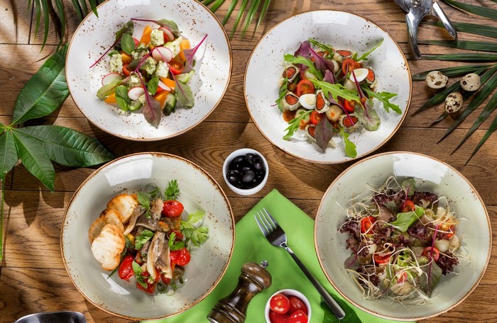 Four salads on a wooden table with palm leaves