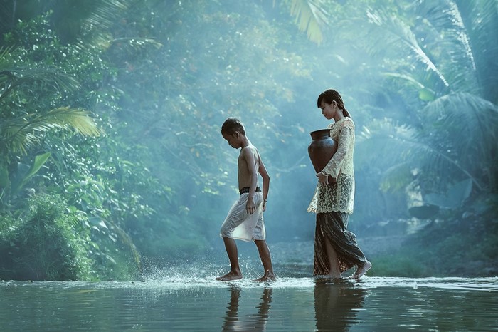 Children carrying water jug through river in jungle