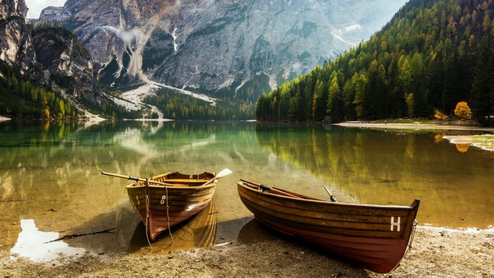 Two wooden boats on a lake with mountains and forests