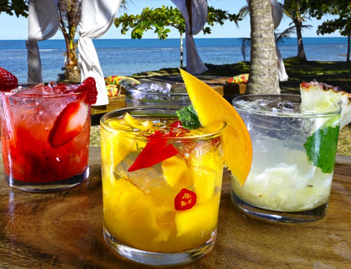 Three colorful cocktails on a wooden table by the beach