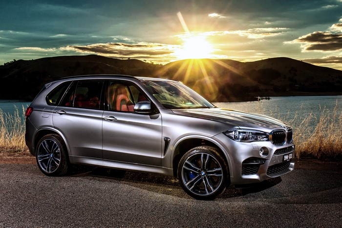 Silver BMW X5 M on a lake shore at sunset