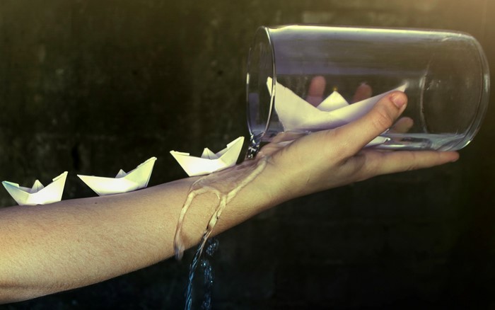Paper boats floating on a person's arm with water pouring from a jar