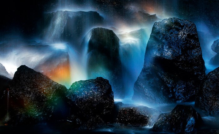 Waterfalls cascading over dark rocks with a rainbow