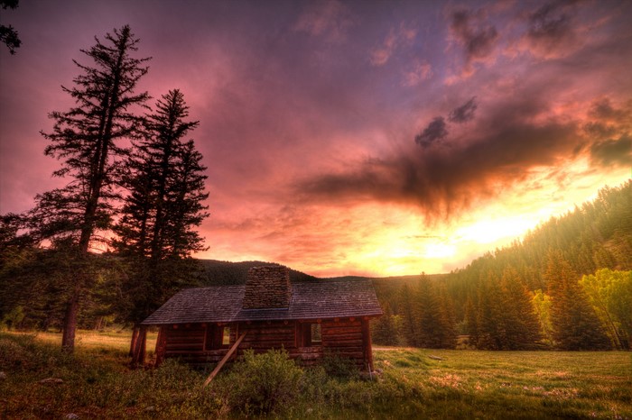 Log cabin in a forest during a dramatic sunset