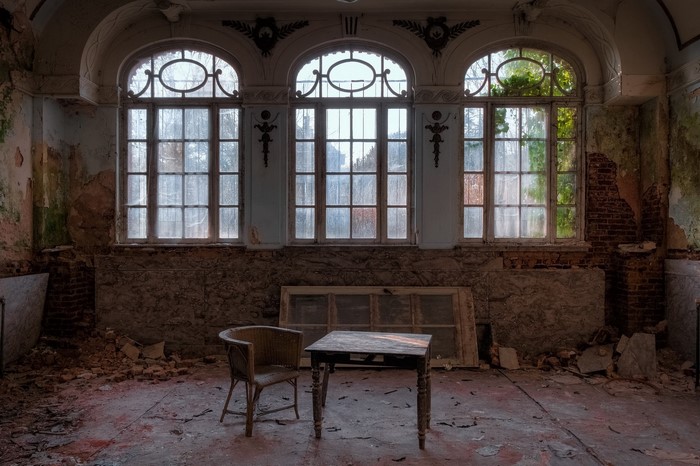 Abandoned room with large windows, chair, and table