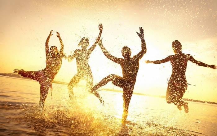 Four people jumping in water with splashes at sunset