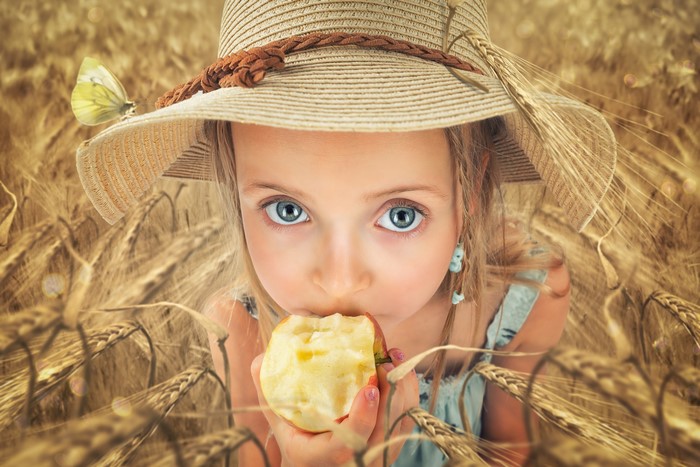 Girl in a hat eating an apple in a wheat field