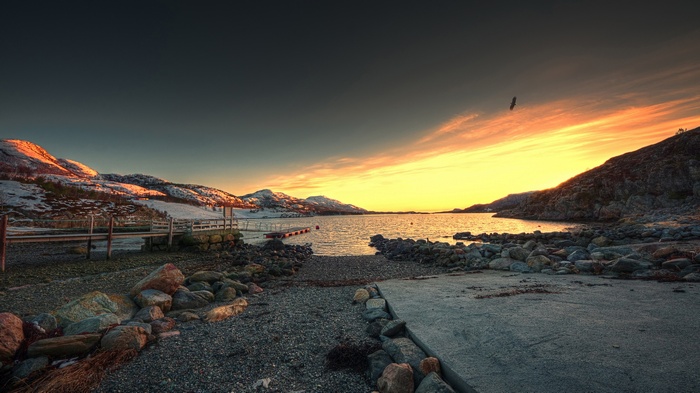 Sunset over a rocky bay with snow-capped mountains