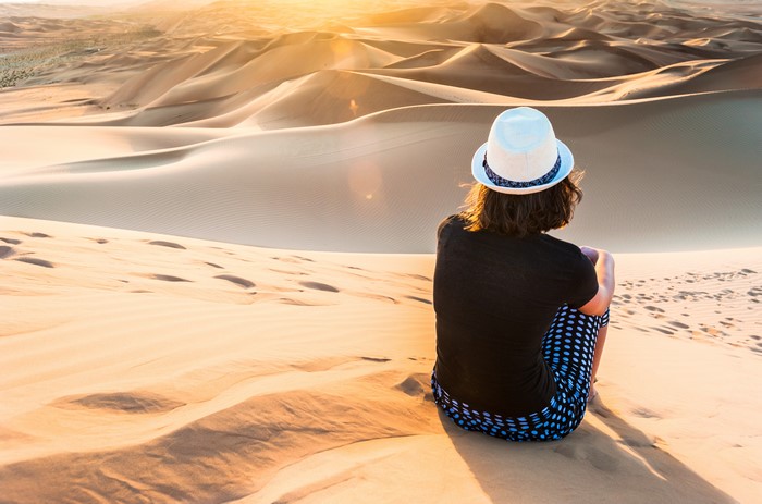 Person in Hat Sitting on Sand Dunes