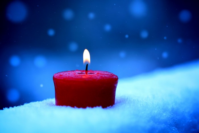 Red candle burning in the snow with bokeh lights