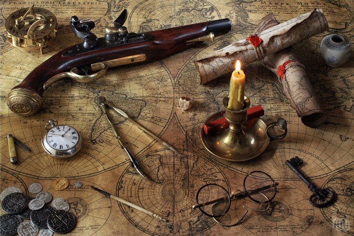 Antique pistol, compass, pocket watch, and maps on a table