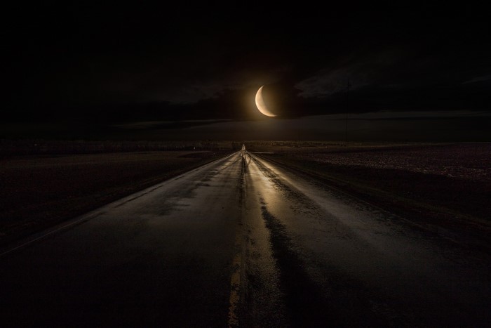 Road at night under a crescent moon