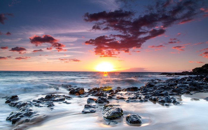 Sunset over the ocean with rocky shore