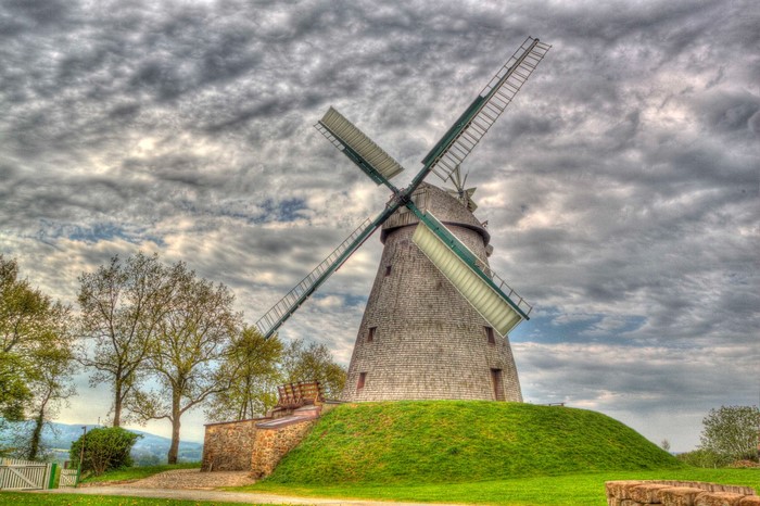 Windmill on a grassy hill under cloudy sky