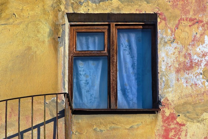 Old window with blue curtains on a weathered wall