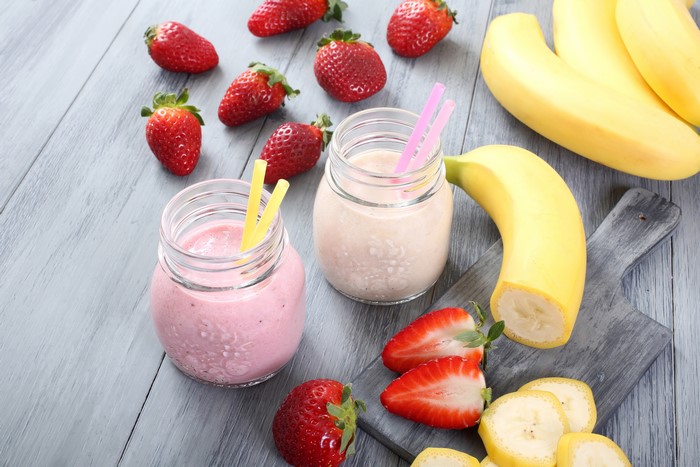 Two jars of strawberry banana smoothies with fresh fruit