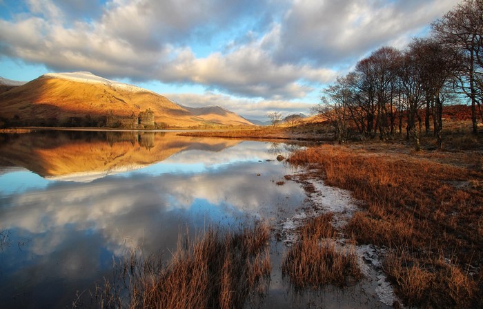 Castle on a lake in Scotland with mountains and autumn colors