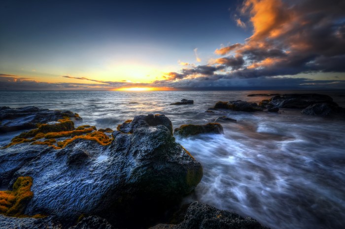 Sunset over the ocean with rocks and clouds