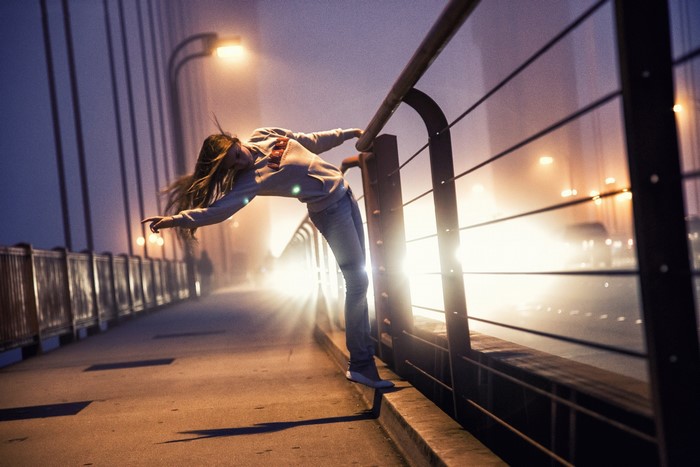 Woman leaning over a bridge railing at night