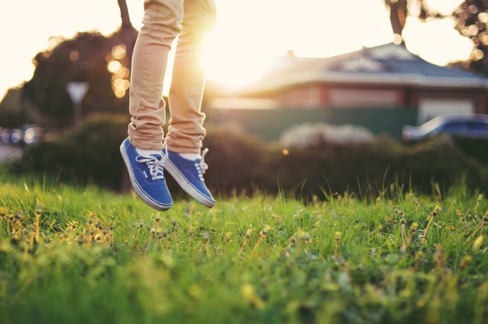 Legs in blue athletic shoes jumping over grass