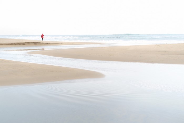 Person in red coat walking on a beach by the sea