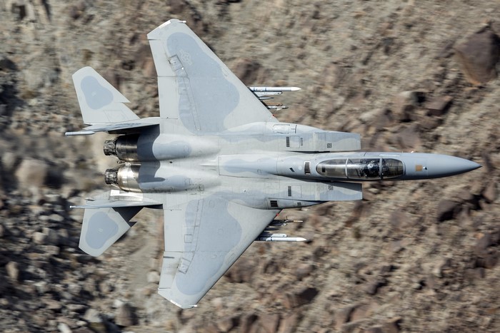 F-15 Eagle fighter jet flying over rocky terrain