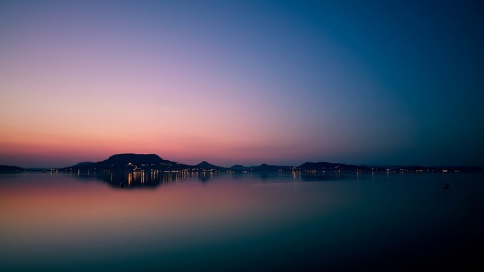 Calm lake at sunset with distant hills and lights