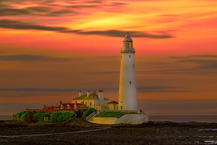White lighthouse on rocky island at sunset