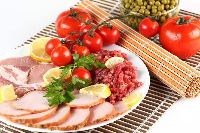 Plate of sliced ham, raw ground meat, tomatoes, lemons, and peas